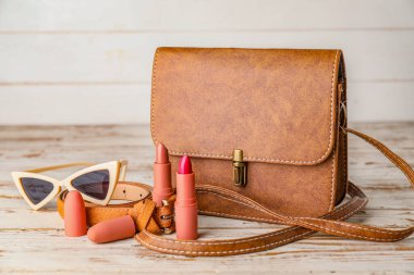 Beyaz ahşap arka planda kadın aksesuarları olan şık bir çanta.