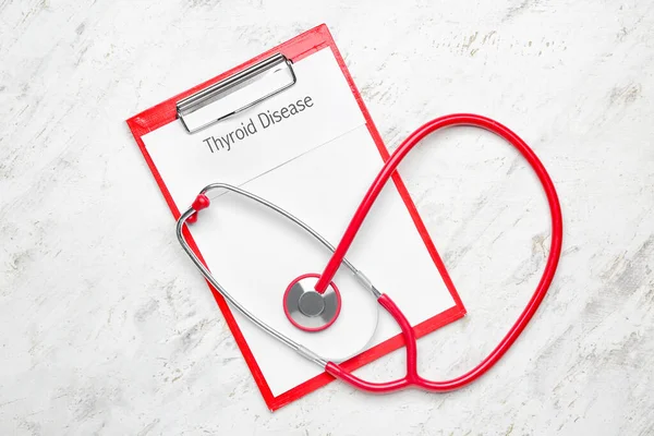 Clipboard with text THYROID DISEASE and stethoscope on white background