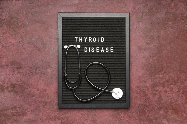 Board with text THYROID DISEASE and stethoscope on color background