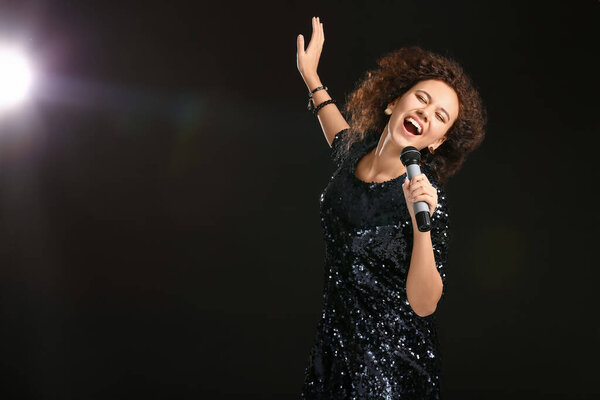 Young African-American woman singing on dark background