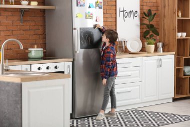 Küçük çocuk mutfakta tahtaya resim çiziyor.