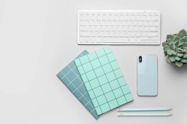 Not defterleri, cep telefonu ve beyaz arkaplanda kalemleri olan bilgisayar klavyesi