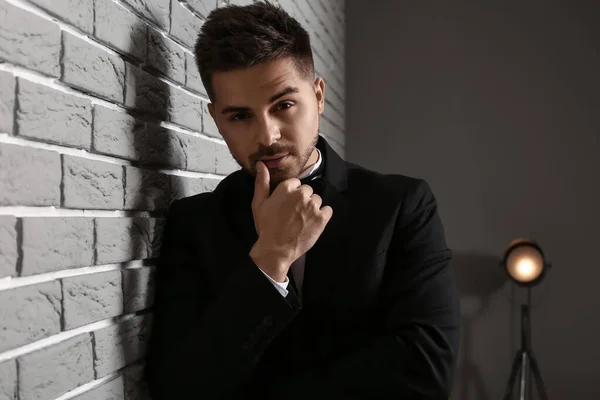 Handsome young man in elegant suit near brick wall