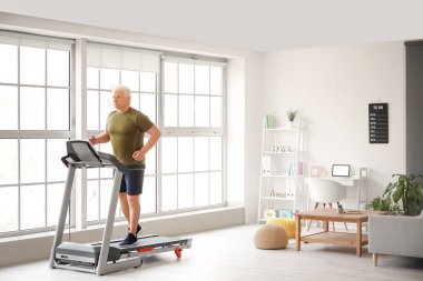 Kıdemli adam evde koşu bandında antrenman yapıyor.
