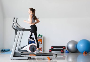 Spor salonundaki koşu bandında antrenman yapan genç bir kadın.