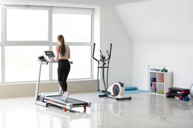 Spor salonundaki koşu bandında antrenman yapan genç bir kadın.