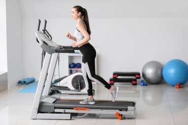 Spor salonundaki koşu bandında antrenman yapan genç bir kadın.