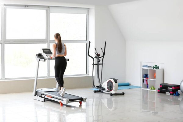 Sporty young woman training on treadmill in gym