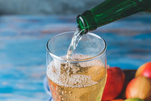 Pouring of apple cider into glass on table