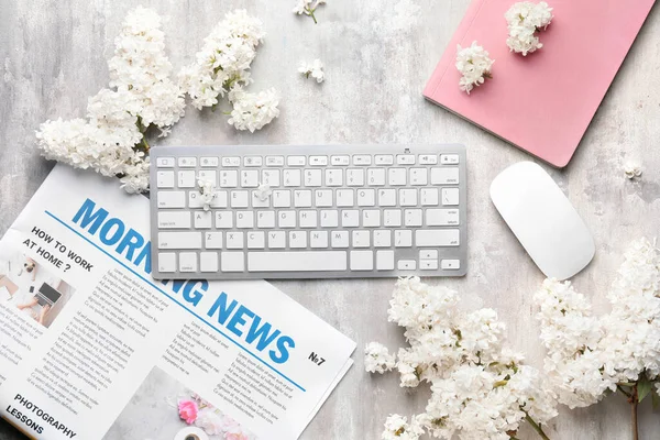 Composition with beautiful lilac flowers, PC keyboard and newspaper on light background