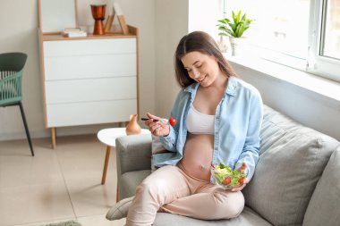 Güzel hamile kadın evde salata yiyor.