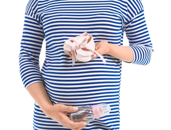 白い背景に赤ちゃんの靴とボトルを持つ美しい妊婦 — ストック写真