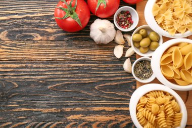 Ahşap arka planda farklı pişmemiş makarna, sebze ve baharatlar.