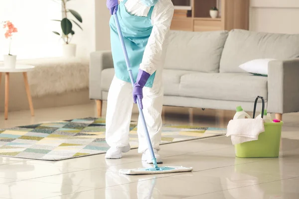 Housewife in protective costume cleaning floor in room