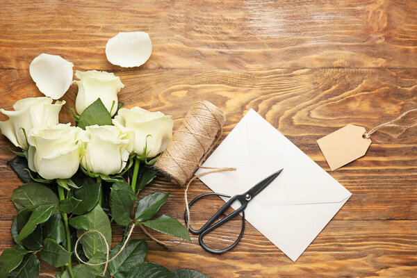 Beautiful white roses, envelope, thread and scissors on wooden background