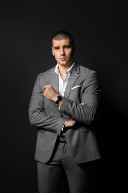 Siyah arka planda zarif takım elbiseli yakışıklı bir genç.