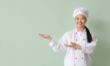 Güzel Asyalı şef renkli arka planda bir şeyler gösteriyor.