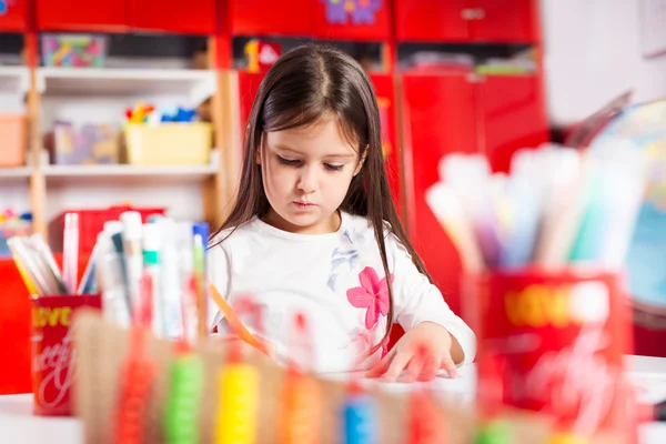 Mała dziewczynka, opierając się na jej książki i zabawy w playtable — Zdjęcie stockowe