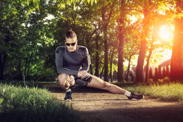 Jovem fitness homem corredor esticando pernas antes de correr — Fotografia de Stock