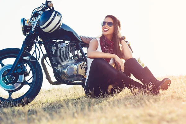 Mulher bonita motociclista sentado ao lado de sua motocicleta em uma estrada . — Fotografia de Stock