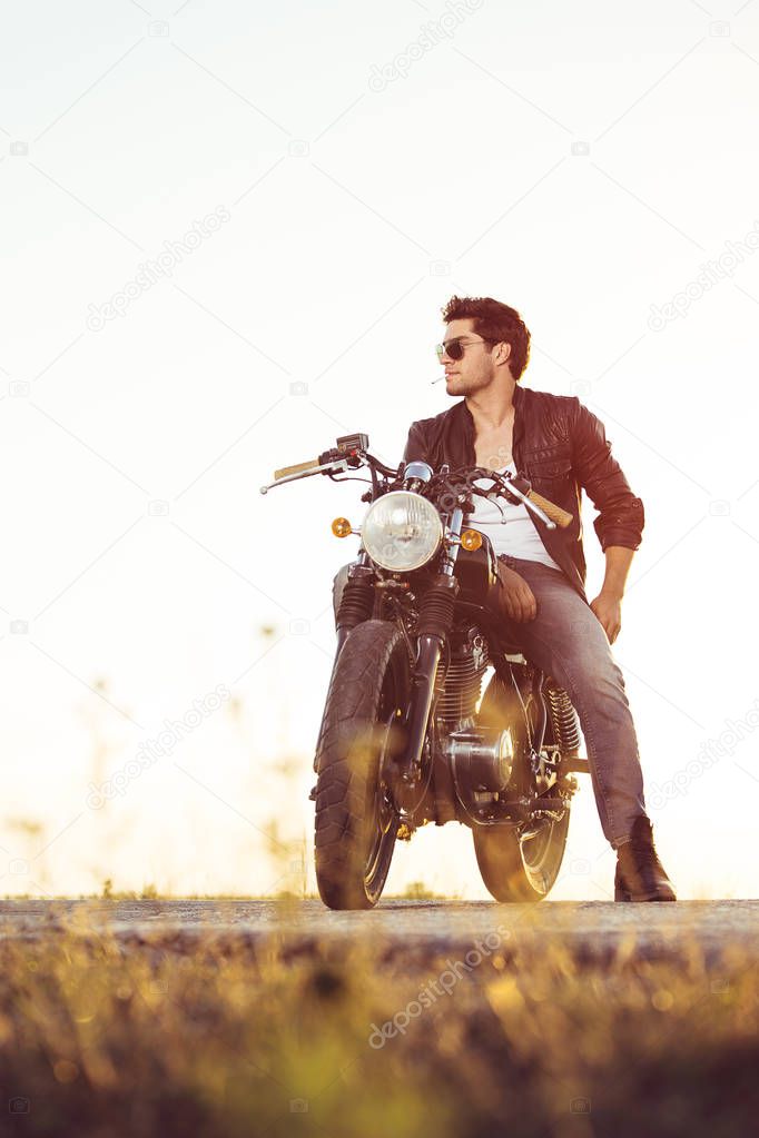 Biker sitting on vintage custom motorcycle. Outdoor lifestyle portrait