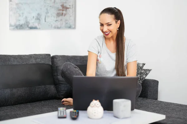 Feliz mujer hermosa casual trabajando en un ordenador portátil sentado en la cama en la casa. — Foto de Stock