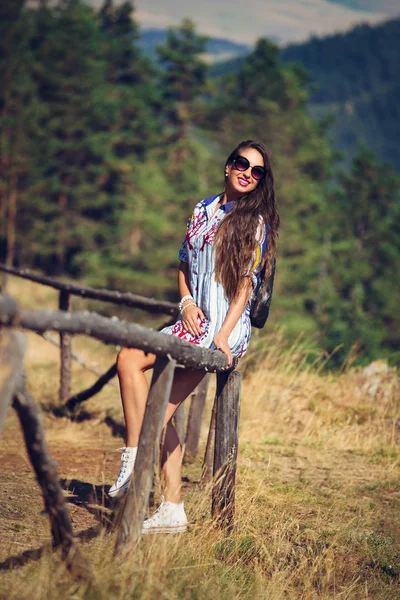 Hermosa chica se sienta en la valla, viaja por las montañas —  Fotos de Stock