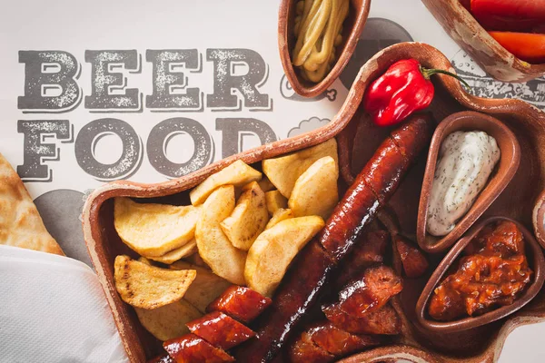 Cerveza y merienda. Variedad de cervezas, embutidos a la parrilla, patatas fritas, saladas sobre fondo de madera — Foto de Stock