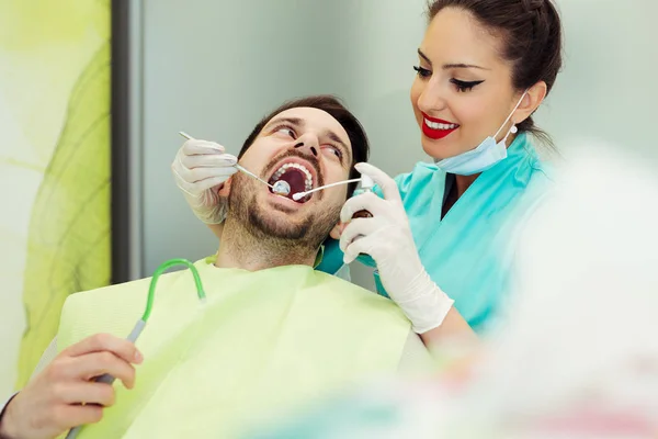 Kvinnliga tandläkare undersöker och arbetar på manlig patient — Stockfoto