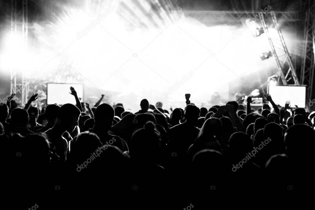 Silhouettes of people at a concert in front of the scene in bright light. Black and White