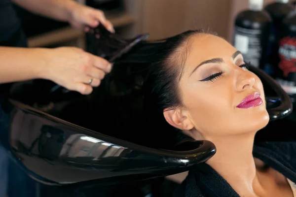 Krásná mladá žena s kadeřnicí mytí hlavy v kadeřnictví — Stock fotografie