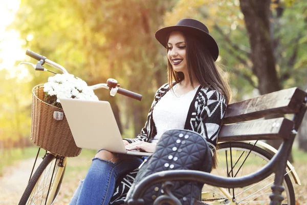 Fiatal nő használ laptop egy parkban a napsütéses őszi napon — Stock Fotó