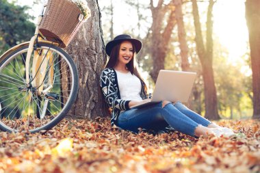 Genç kadın bir parkta güneşli bir sonbahar gününde laptop kullanıyor