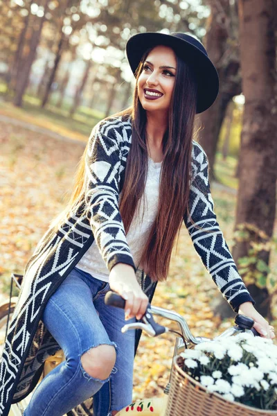 Beautiful woman pushing a bicycle with a bouquet in it outdoor — Stock Photo, Image