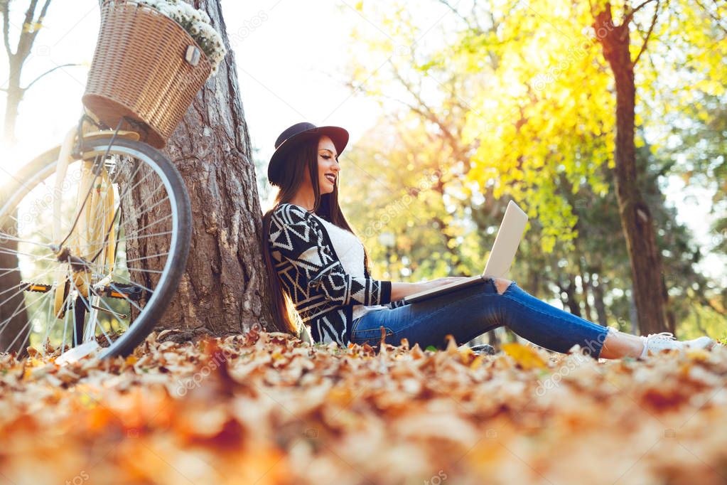 Young woman is using laptop in a park on a sunny autumn day