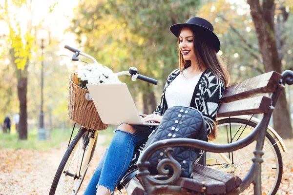 Young woman is using laptop in a park on a sunny autumn day — Stock Photo, Image