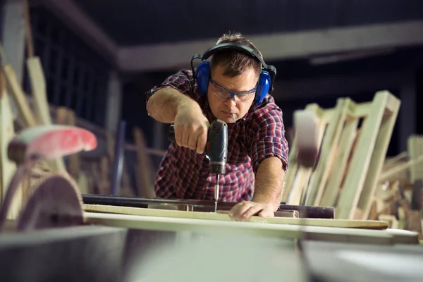 Tischler mit Elektrobohrmaschine bohrt Holzbrett in Werkstatt — Stockfoto