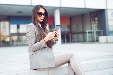 Merdivenlerde tablet bilgisayarlı bir iş kadını oturuyor.