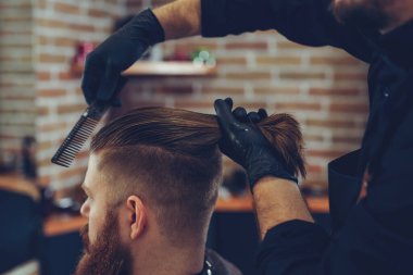 Creating new hair look. Young bearded man getting haircut by hairdresser.