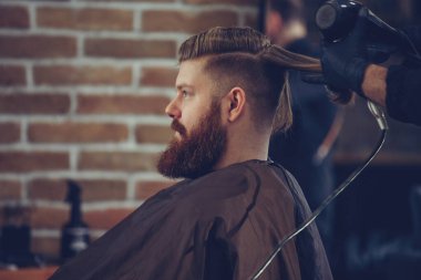 Creating new hair look. Young bearded man getting haircut by hairdresser.
