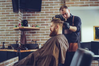 Creating new hair look. Young bearded man getting haircut by hairdresser.