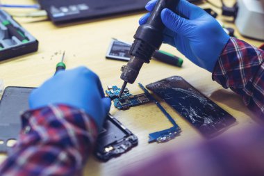 Laboratuvarda akıllı telefonun ana kartını tamir eden teknisyen. Cep telefonu onarım süreci gösteriliyor.