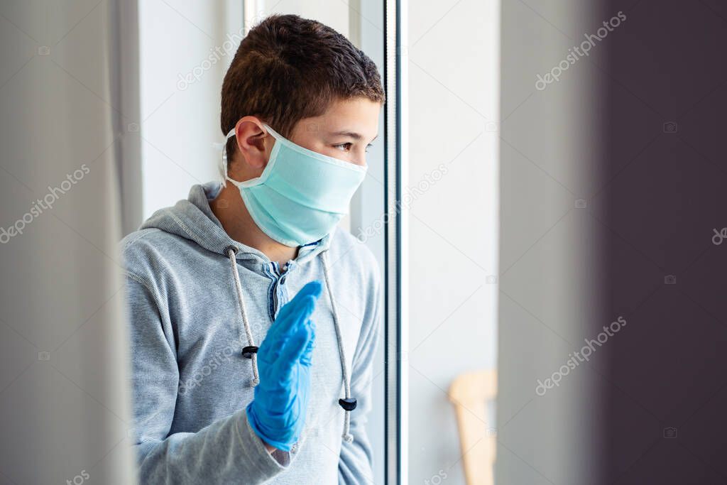 School age boy in a surgeon protection mask sitting by the window . Patient isolated to prevent infection. 