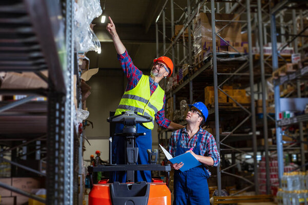 Workers in logistics warehouse at forklift checking list.