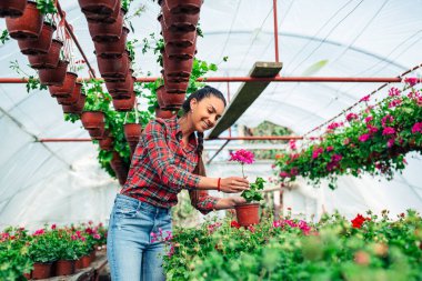 Bir serada saksı çiçeği tutan gülümseyen genç bir kadın..