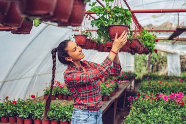 Bir serada saksı çiçeği tutan gülümseyen genç bir kadın..