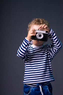 Gri bir arka plan - studio fotoğraf üzerinde bir kamera küçük kıvırcık saçlı çocuk. Fotoğraf çekmek çocuk öğrenir. 