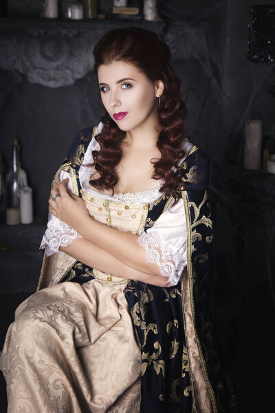 Beautiful woman in an old dress with a train. Vintage furnishings, historic vintage image. The girl with white skin, red lips and beautiful wavy hair. 