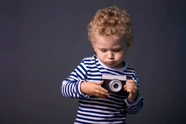 Pequeno Rapaz Cabelos Encaracolados Com Uma Câmera Fundo Cinza Uma — Fotografia de Stock