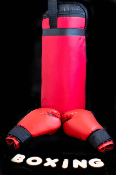 Red boxing gloves, boxing bag for punches and the inscription of the wooden letters \